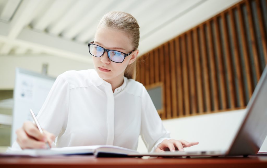 Diligent student or young specialist writing down working plan or financial notes.