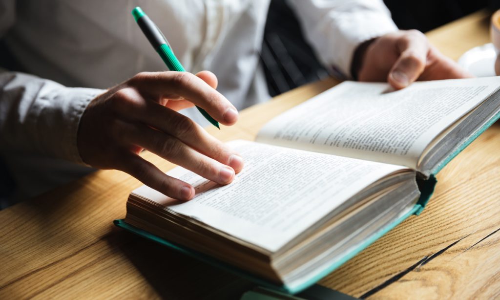 Cropped photo of man in white shirt reading book.