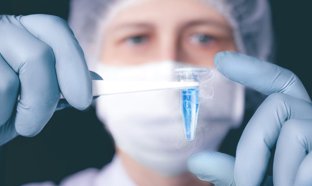 Scientist or tech holds liquid biological sample in gloved hands.