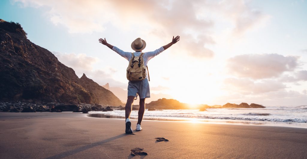 Young man arms outstretched by the sea at sunrise enjoying freedom and life, people travel wellbeing concept.