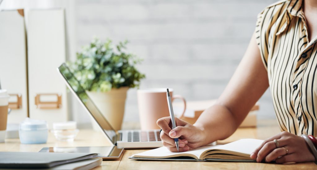 Close-up image of business woman writing down her ideas in notepad.