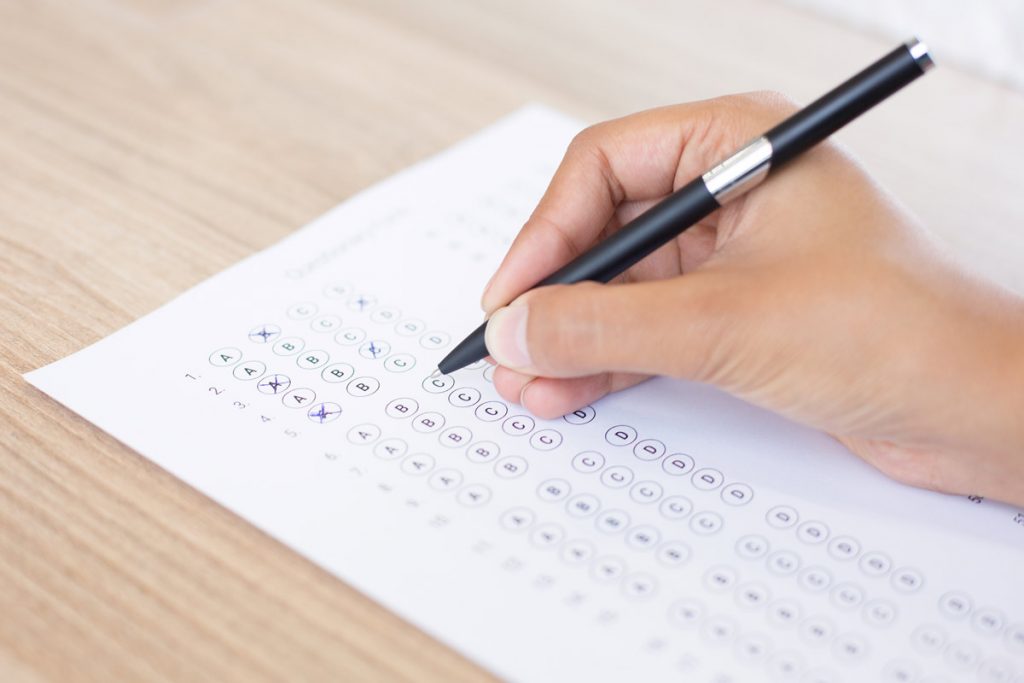 Closeup of hand holding pen and filling out questionary form on table.