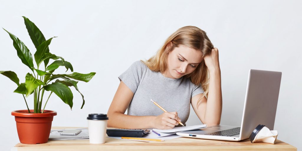 Portrait of serious blonde young businesswoman looking with pencil in her notebook.