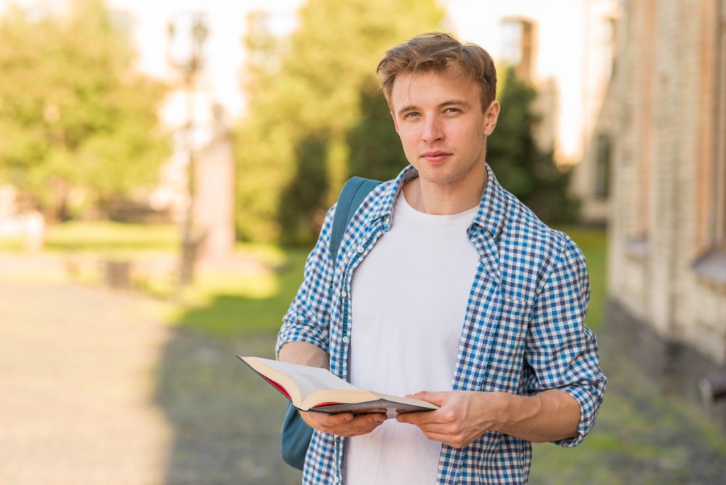 School boy with book in park.