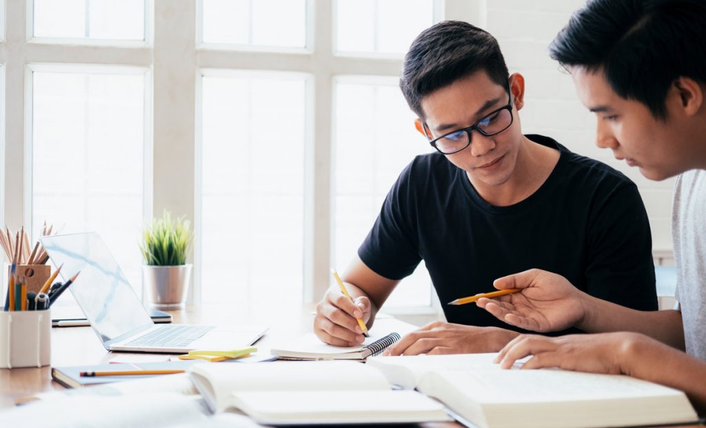 Learning, education and school concept. Young men studying for a test or an exam. Tutor books with friends. Young students campus helps friend catching up and learning.