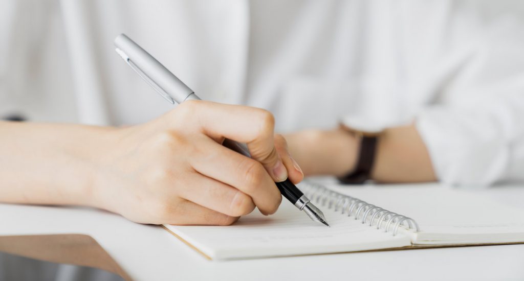 Close-up of hand writing on blank notebook on table in house.