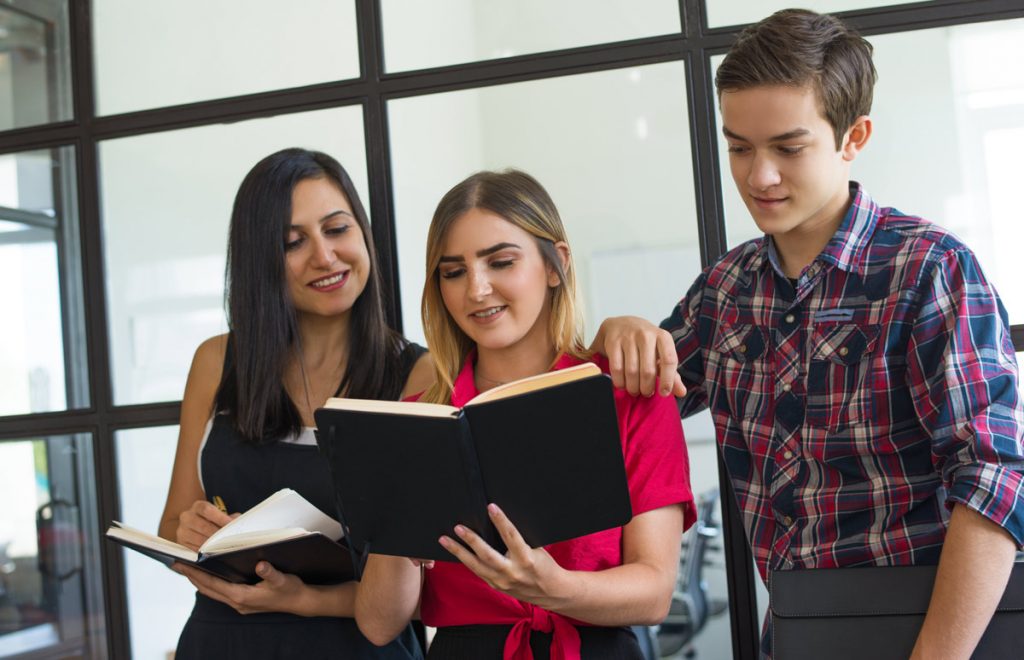 Portrait of happy young students sharing homework at college. Two Caucasian girl and boy standing together, reading notes or doing homework together.