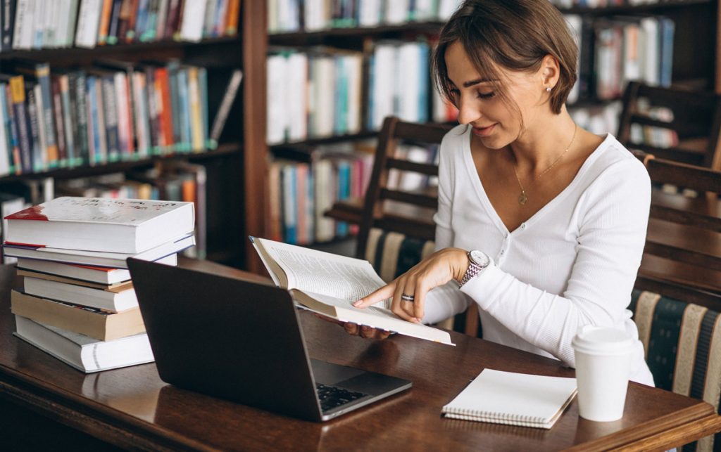 Young woman sitting at the library using books and computer.