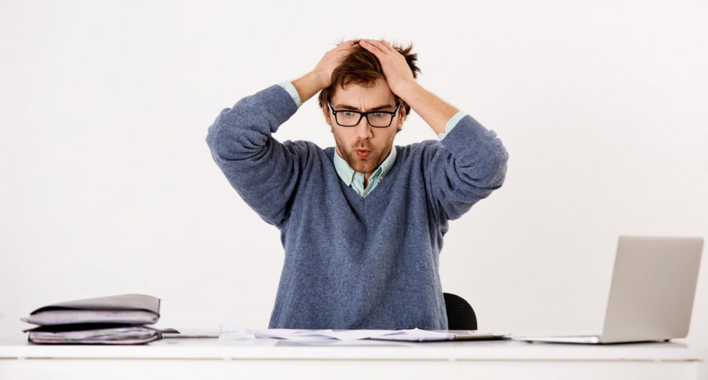 Handsome tired young businessman in glasses sitting at the office desk with hands over his head.