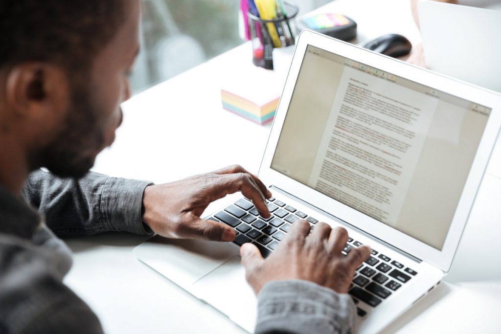 Cropped photo of serious young man sitting in office coworking. Looking aside using laptop computer. Focus on computer.