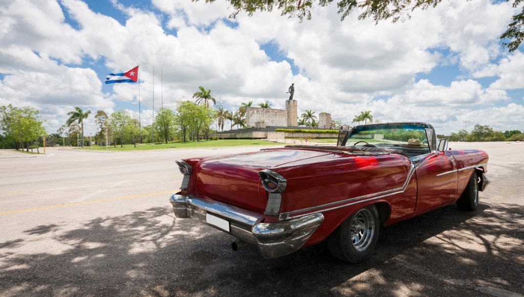 Classic convertible car with monument and cuban flag in background.