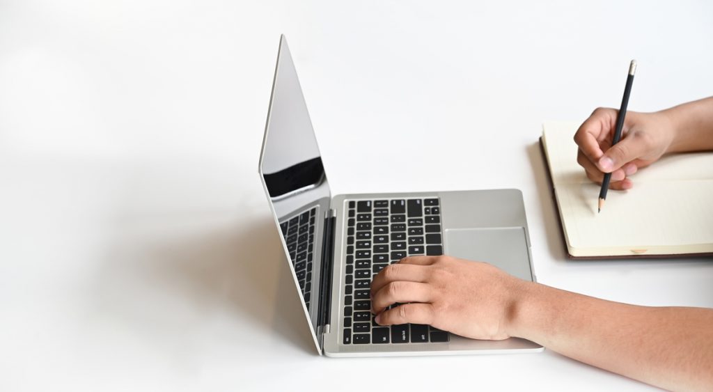 Hands using laptop and writing notebook paper with copy space table.