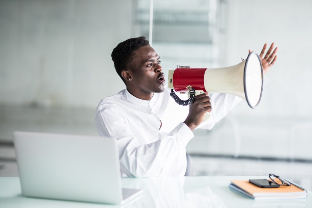 Afro businessman yelling through a megaphone in the office.