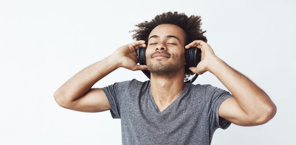 Happy african man smiling listening to music in headphones. White background. Closed eyes.